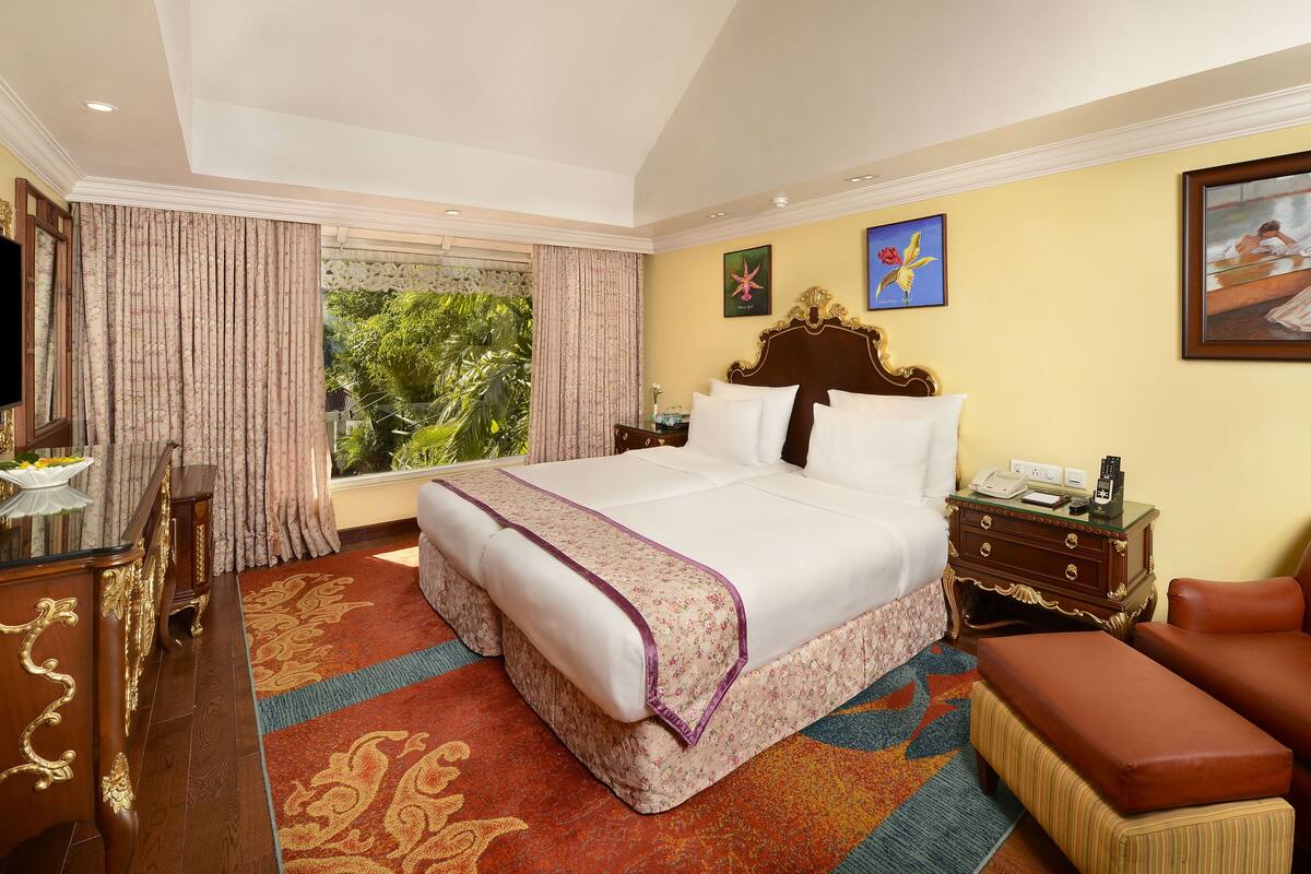 A spacious hotel room with a large bed, a sitting area, a desk, and a view of greenery.