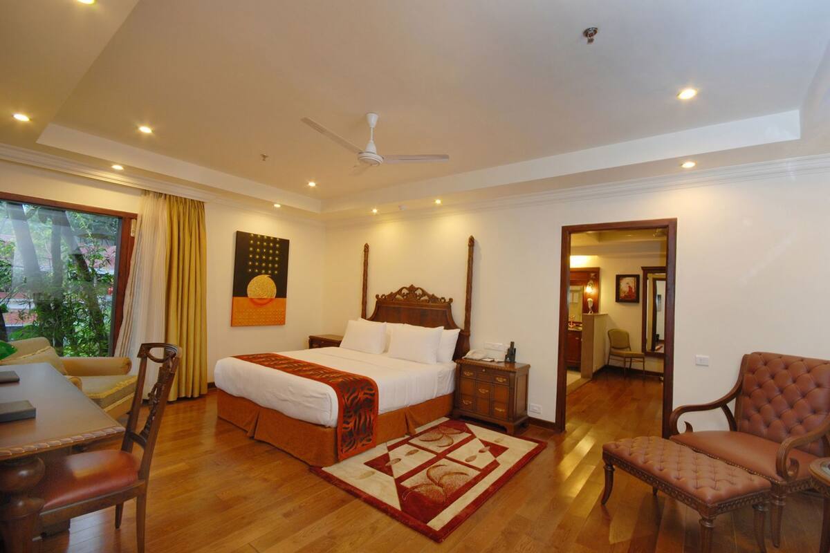 A hotel room with a bed, a desk, a chair, a ceiling fan, and a view of the outdoors.
