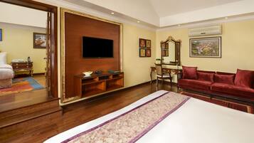 A hotel room with a large bed, a TV mounted on a wooden panel, a red sofa, a mirror, and a wooden cabinet.