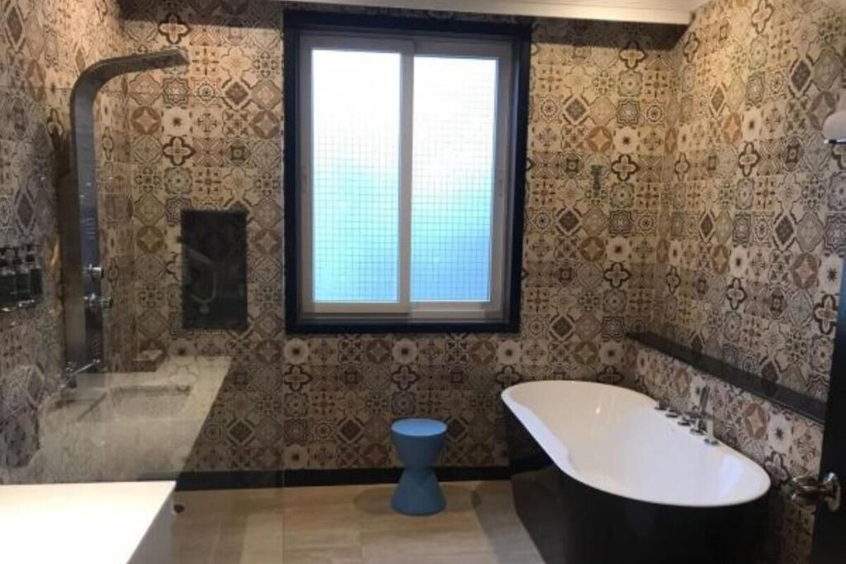 Un bagno con carta da parati decorata, un'ampia finestra, una vasca da bagno indipendente e un box doccia.