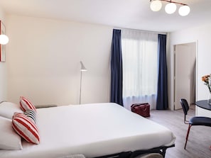 A hotel room with a bed, a desk, a chair, a lamp, and a view of the outdoors through the window. - Aparthotel Adagio Access Nantes Viarme (Nantes)