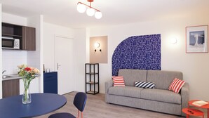 A modern living room with a grey sofa, two chairs, a dining table, and a kitchen area with a microwave. - Aparthotel Adagio Access Nantes Viarme (Nantes)