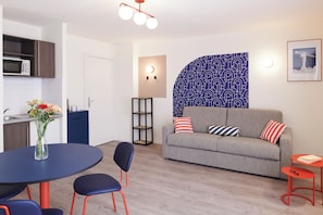 A modern living room with a grey sofa, two chairs, a dining table, and a kitchen area with a microwave. - Aparthotel Adagio Access Nantes Viarme (Nantes)