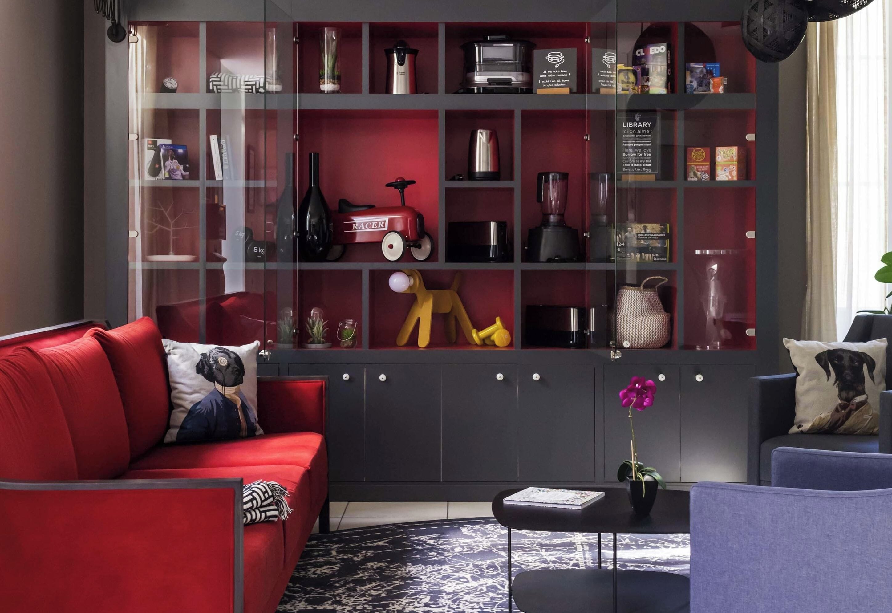 Uma sala de estar moderna com um sofá vermelho, uma mesa de centro preta e uma estante cheia de diversos objetos.