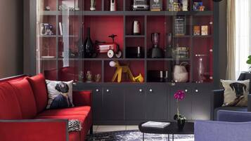 Uma sala de estar moderna com um sofá vermelho, uma mesa de centro preta e uma estante cheia de diversos objetos.
