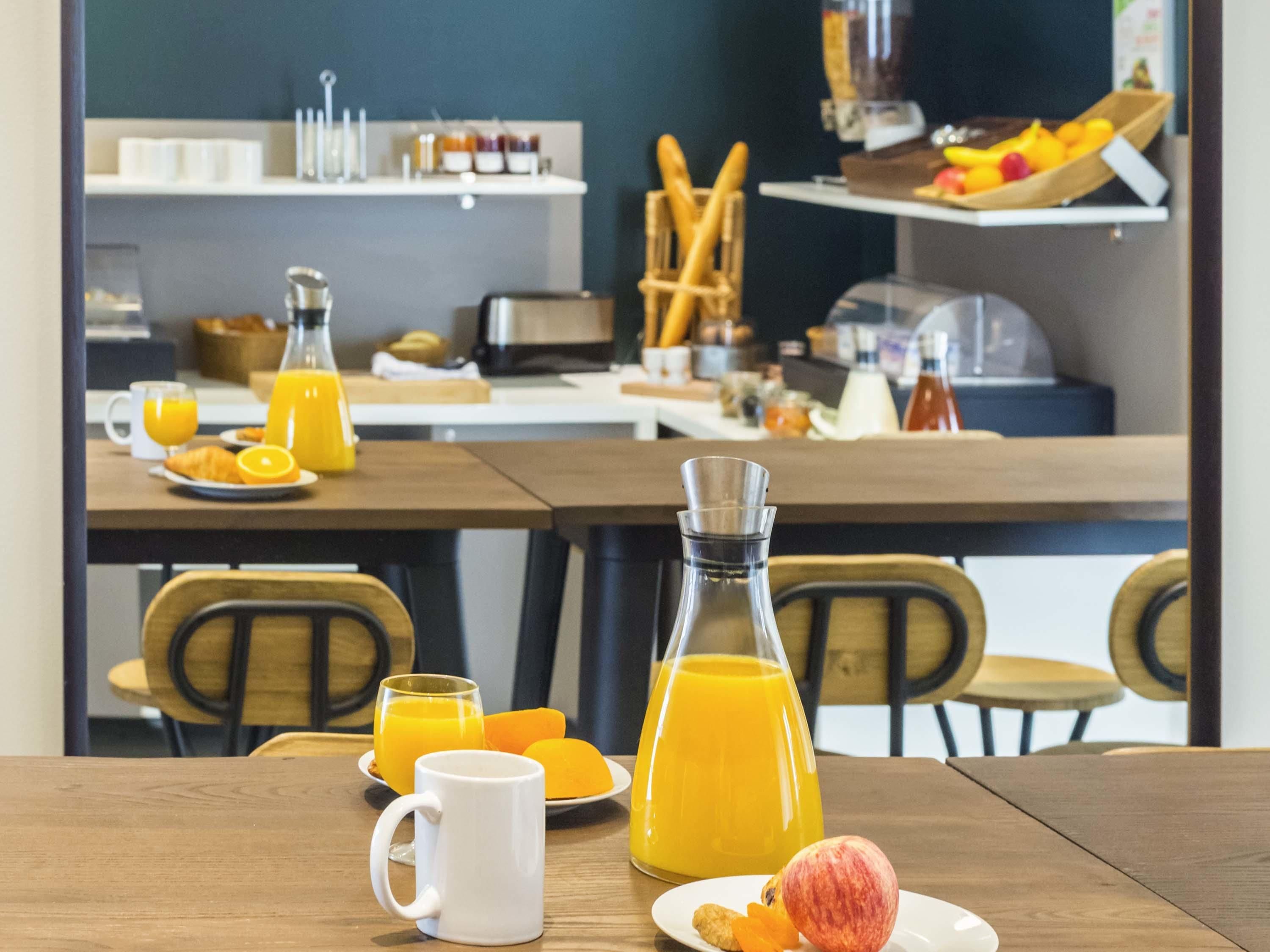 Een ontbijttafel met stoelen, een fles sinaasappelsap, een mok en een bord met fruit.