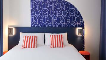 A hotel room with a bed, two pillows, a headboard, bedside lamps, and a wall with a geometric pattern.