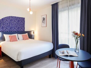 Ein Hotelzimmer mit einem Bett, einem Nachttisch und einem kleinen runden Tisch mit Buch und Blumen.