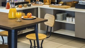 Un moderno comedor con una mesa de madera, sillas y diversas opciones para el desayuno, como frutas, pan y bebidas.