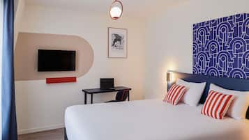 A hotel room with a bed, a desk, a chair, a TV, and a patterned wall.