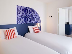Une chambre d’hôtel avec deux lits, un mur décoré de motifs et une porte donnant sur une autre pièce.