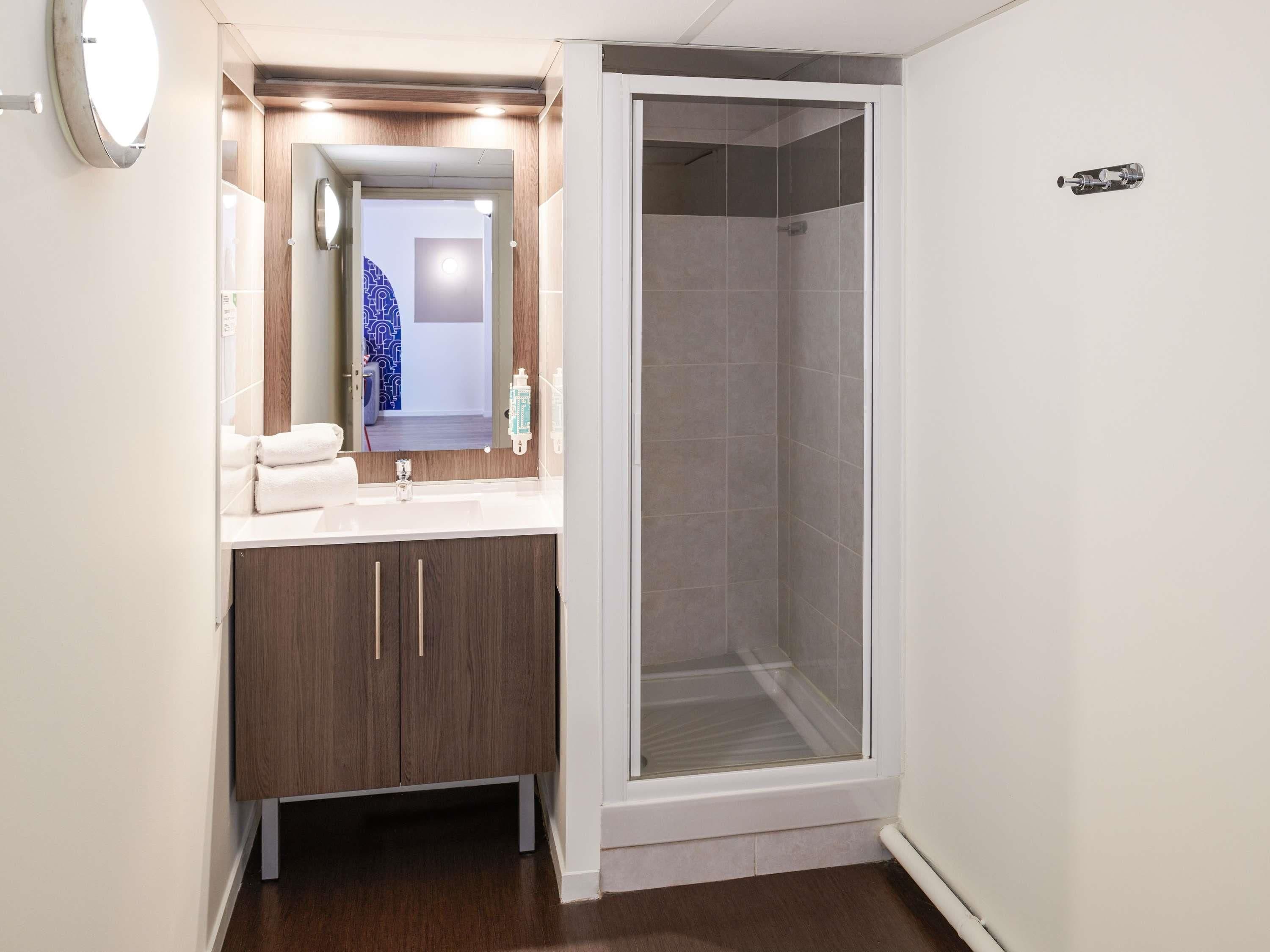 Een moderne badkamer met een douche, een wastafel met spiegel en houten kasten.