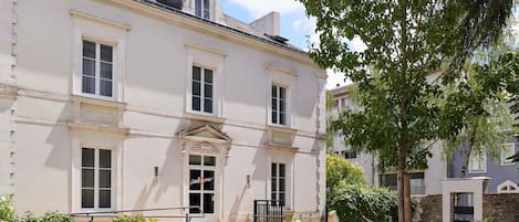 A two-story building with a symmetrical facade, a central entrance with a door, and a small balcony above the main entrance.