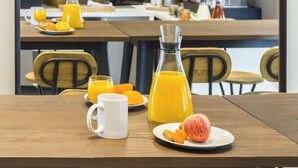 Una mesa de desayuno con jugo de naranja, una taza blanca y un plato con fruta y tostadas.