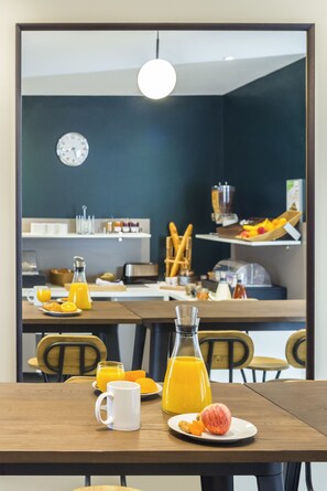 Una mesa de desayuno con jugo de naranja, una taza blanca y un plato con fruta y tostadas.