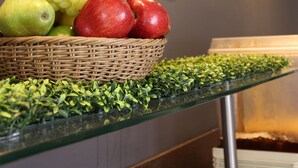 Uma cesta de frutas com uvas e maçãs sobre uma mesa de vidro, em frente a uma parede com as palavras "ibis" e "SLP" visíveis.