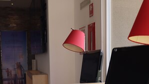 Um escritório moderno com uma escrivaninha de madeira, um laptop e duas lâmpadas vermelhas. Há duas cadeiras brancas com detalhes em vermelho e uma janela grande ao fundo.