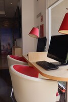Un espacio de oficina moderno con un escritorio de madera, una computadora portátil y dos lámparas rojas. Hay dos sillas blancas con detalles rojos y una ventana grande al fondo.