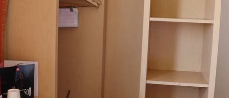 A hotel room with a wooden wardrobe, a desk with a chair, and a hanging coat rack.