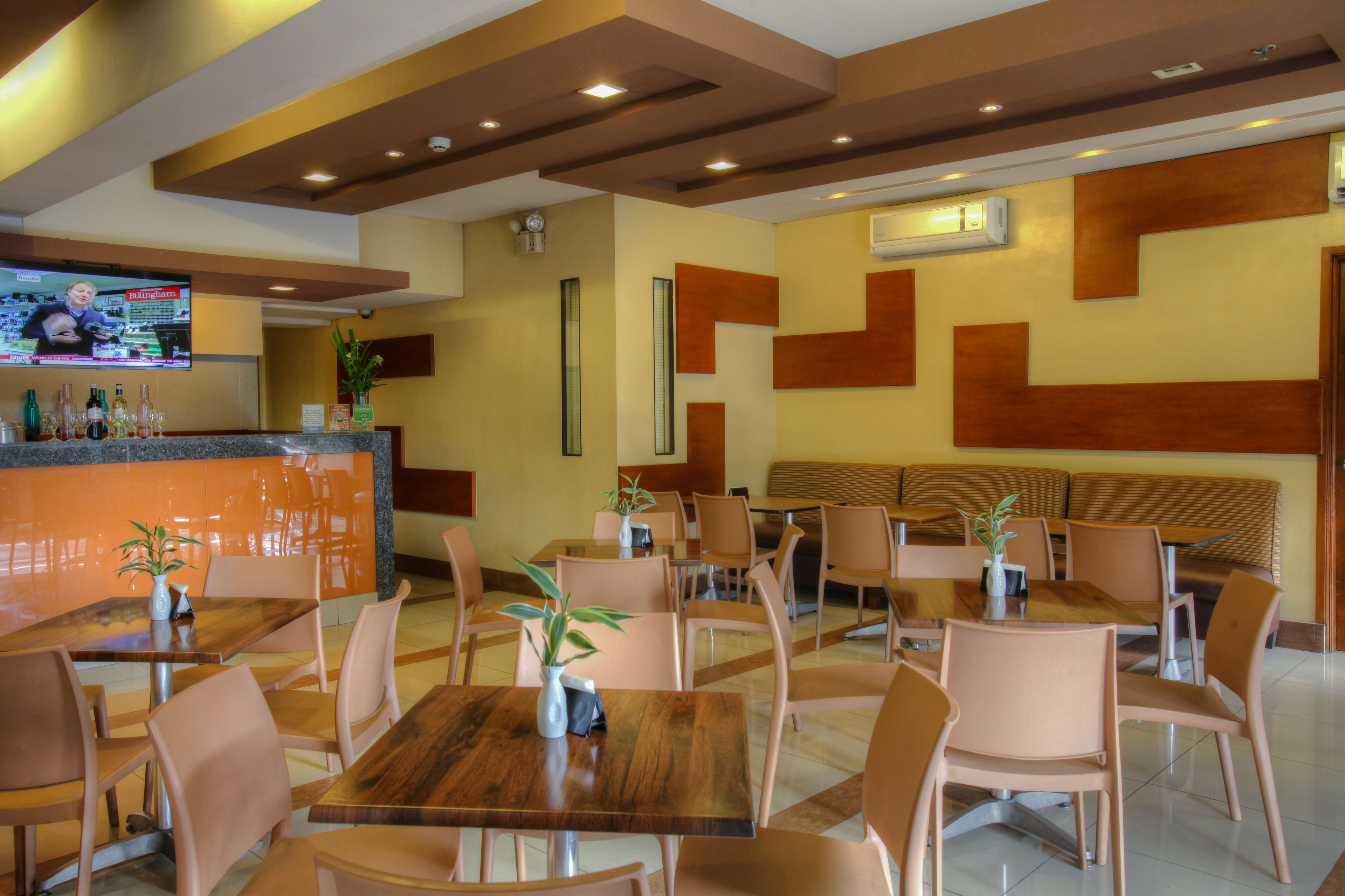 Ein Restaurant mit Holztischen und -stühlen, einer Bar und einem Fernseher, der eine Nachrichtensendung zeigt.
