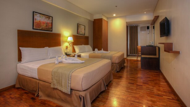 Habitación de hotel con dos camas, un escritorio, una silla, un televisor y obras de arte en las paredes.
