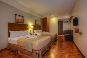 A hotel room with two beds, a desk, a chair, a TV, and artwork on the walls.