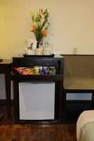 A compact kitchenette with a refrigerator, a coffee maker, a kettle, and a small fridge. There are snacks and drinks on the counter.