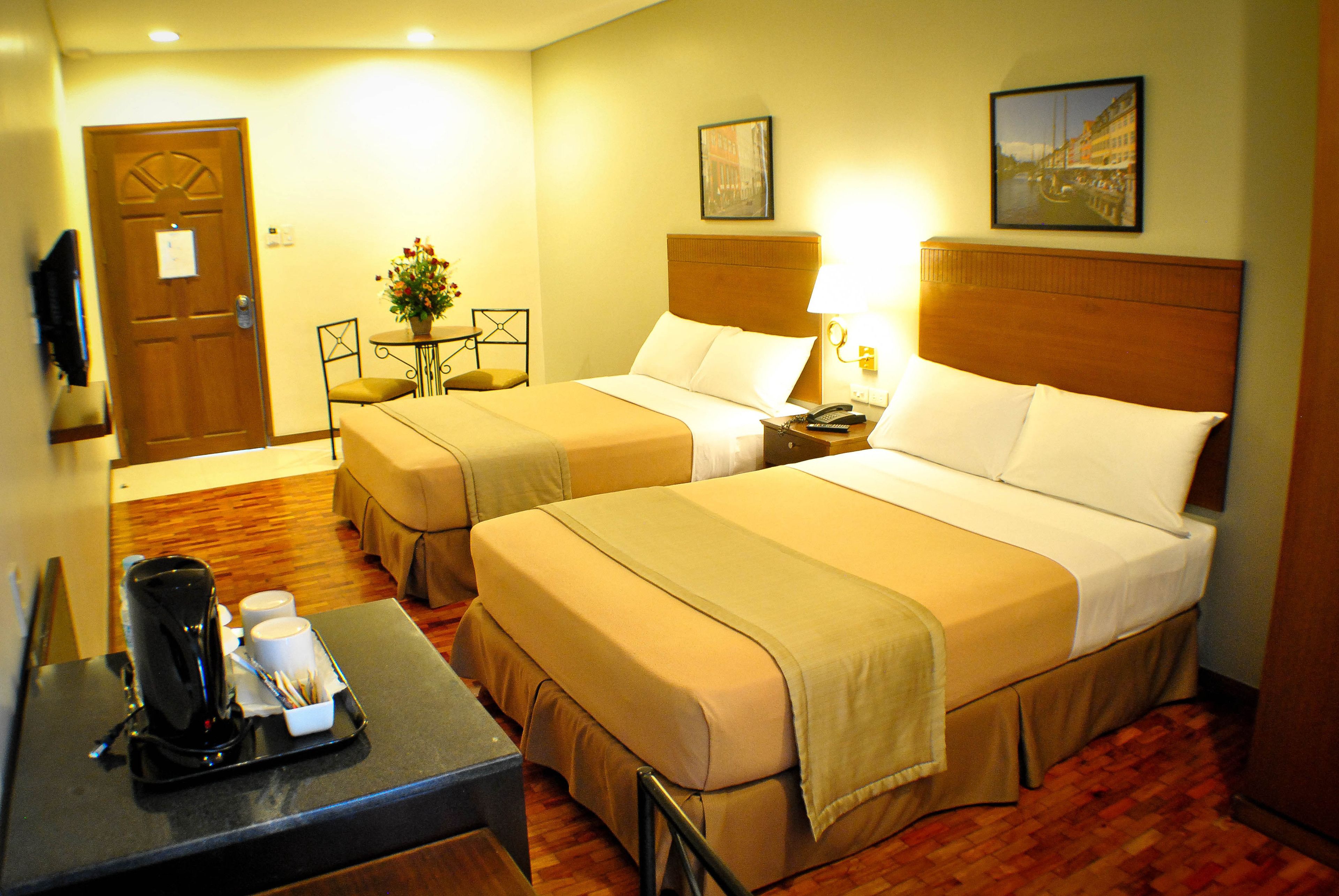 A hotel room with two beds, a coffee maker, a small table, and a door.
