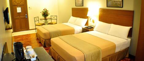 A hotel room with two beds, a coffee maker, a small table, and a door.