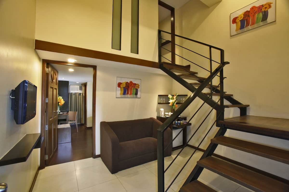 A modern living room with a brown sofa, a wooden staircase, and a dining area in the background.