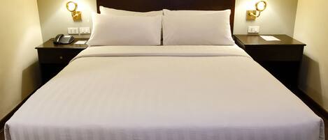 A neatly made bed with white linens, two bedside lamps, and a wooden headboard.