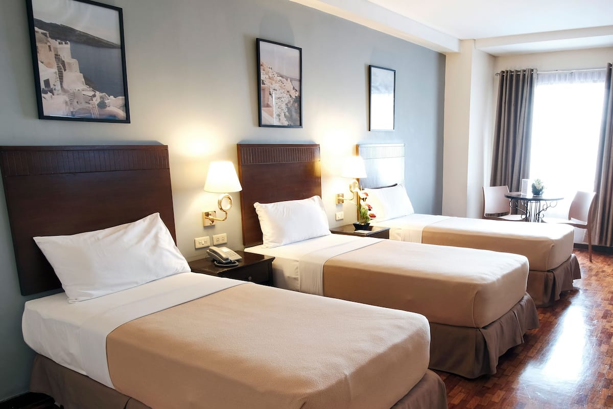 A hotel room with three beds, wooden flooring, and a small table with chairs.