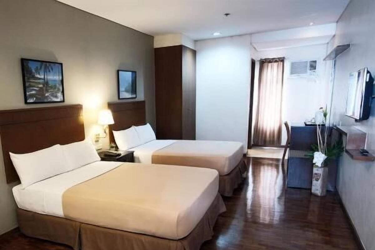 A hotel room with two beds, a desk, a chair, a TV, and a window with curtains.