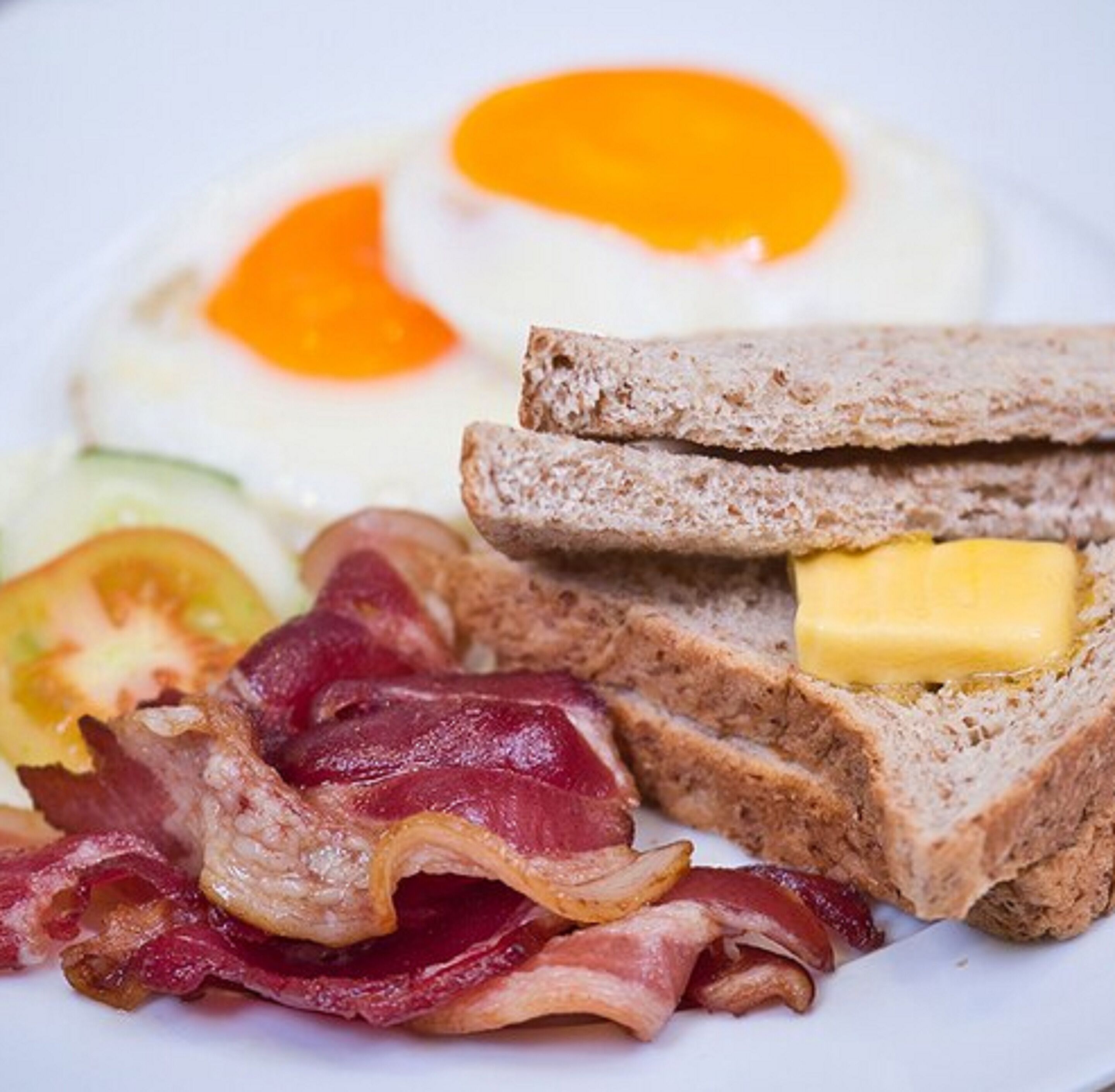 A breakfast plate with eggs, bacon, toast with butter, and a slice of tomato.