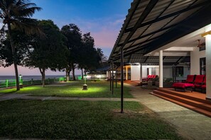 A hotel with a covered outdoor seating area, a pool, and a view of the sea.