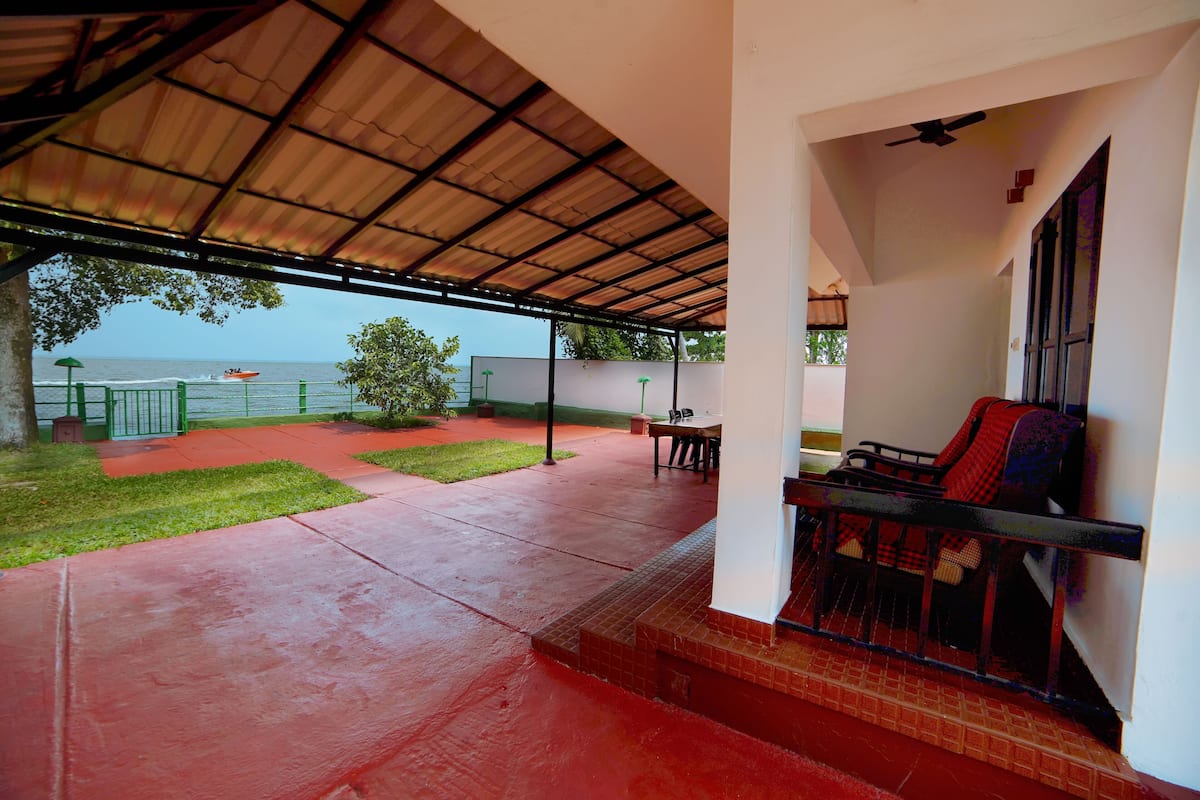 A covered outdoor area with a red floor, a table, chairs, and a view of the sea.