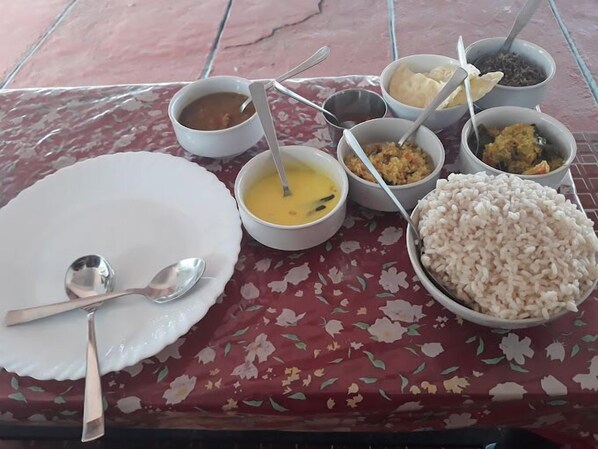 A table set with various dishes including rice, curry, and soup, with a floral tablecloth.