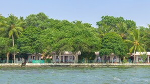 A waterfront hotel with multiple buildings, palm trees, and a clear sky. - ILLIKKALAM Lakeside Cottages Kumarakom Kerala (Kottayam)