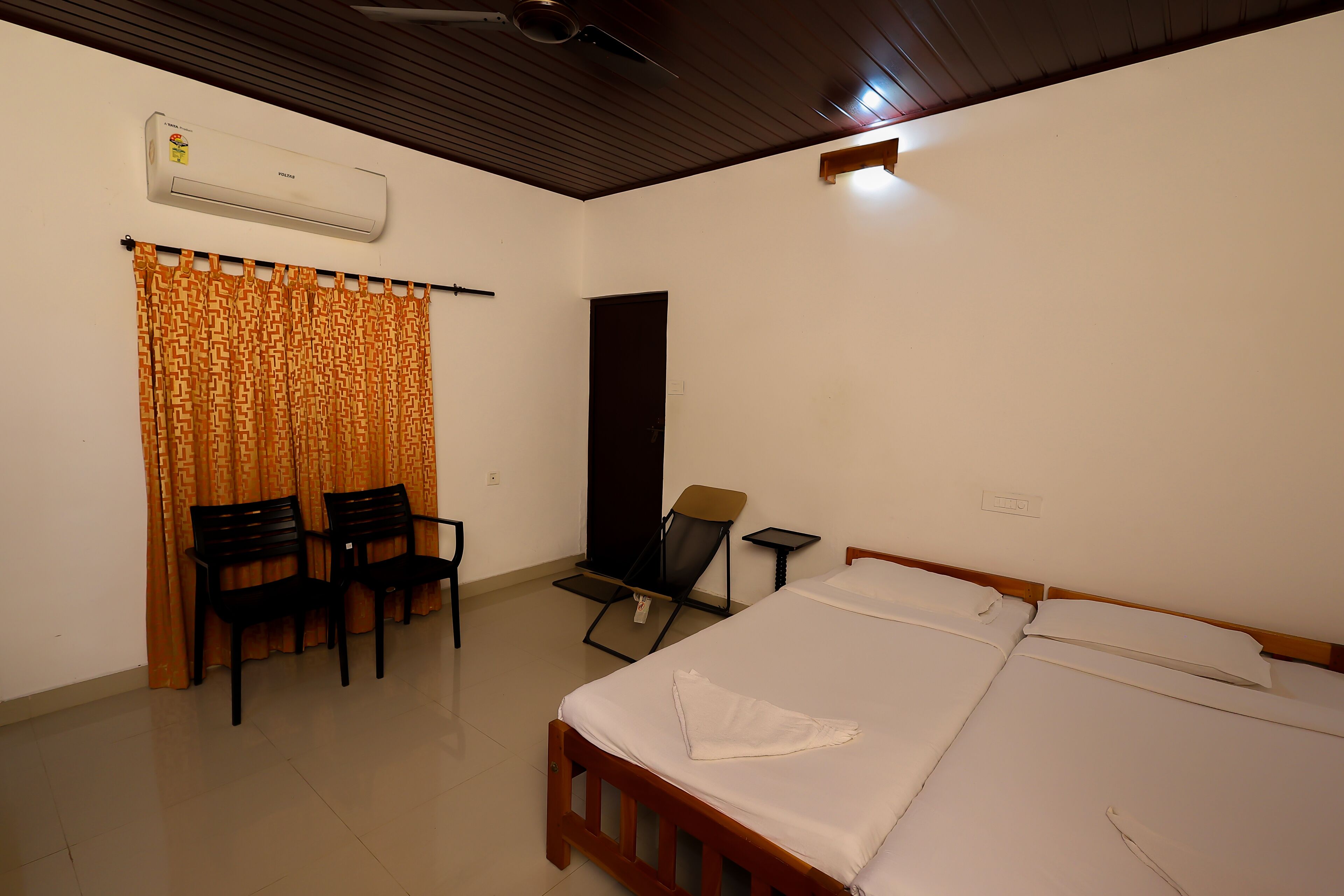 A room with a bed, two chairs, a desk, and an air conditioning unit.