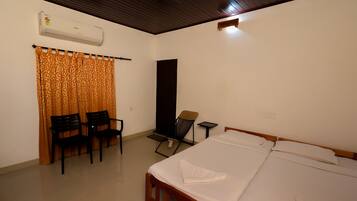 A room with a bed, two chairs, a desk, and an air conditioning unit.