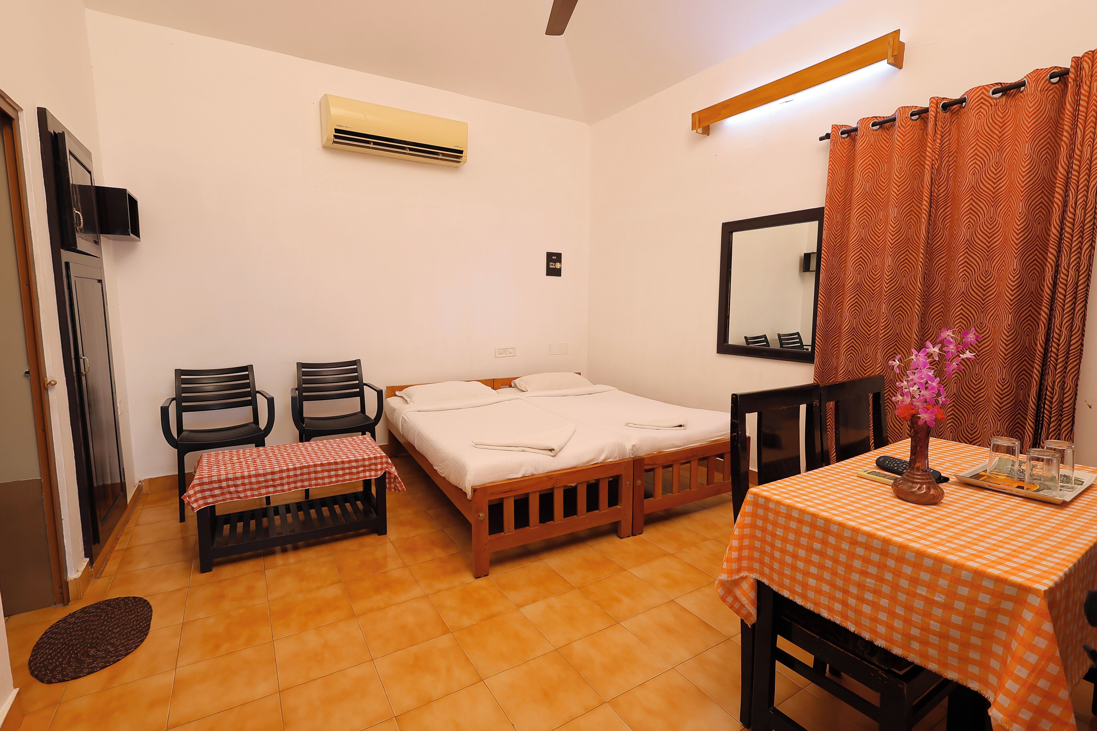 A room with a bed, two chairs, a table with a checkered tablecloth, a mirror, and a curtain.