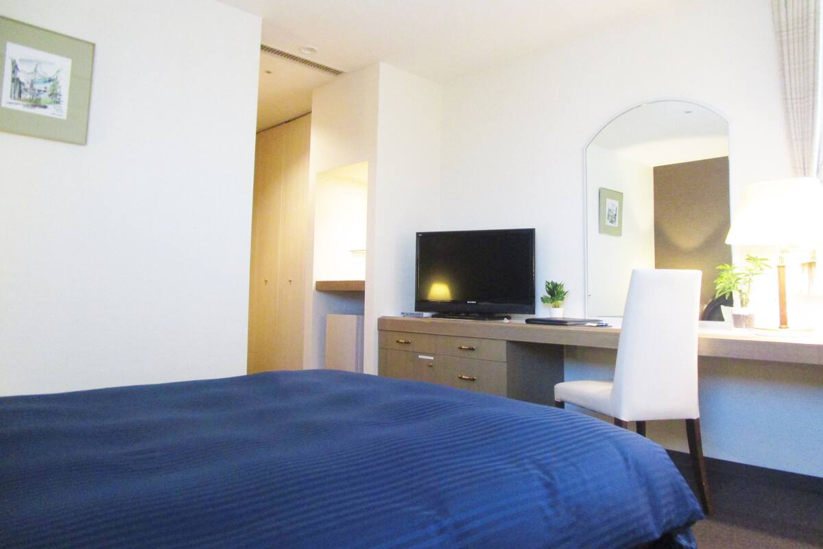 A hotel room with a bed, a desk with a computer, a television, and a chair.
