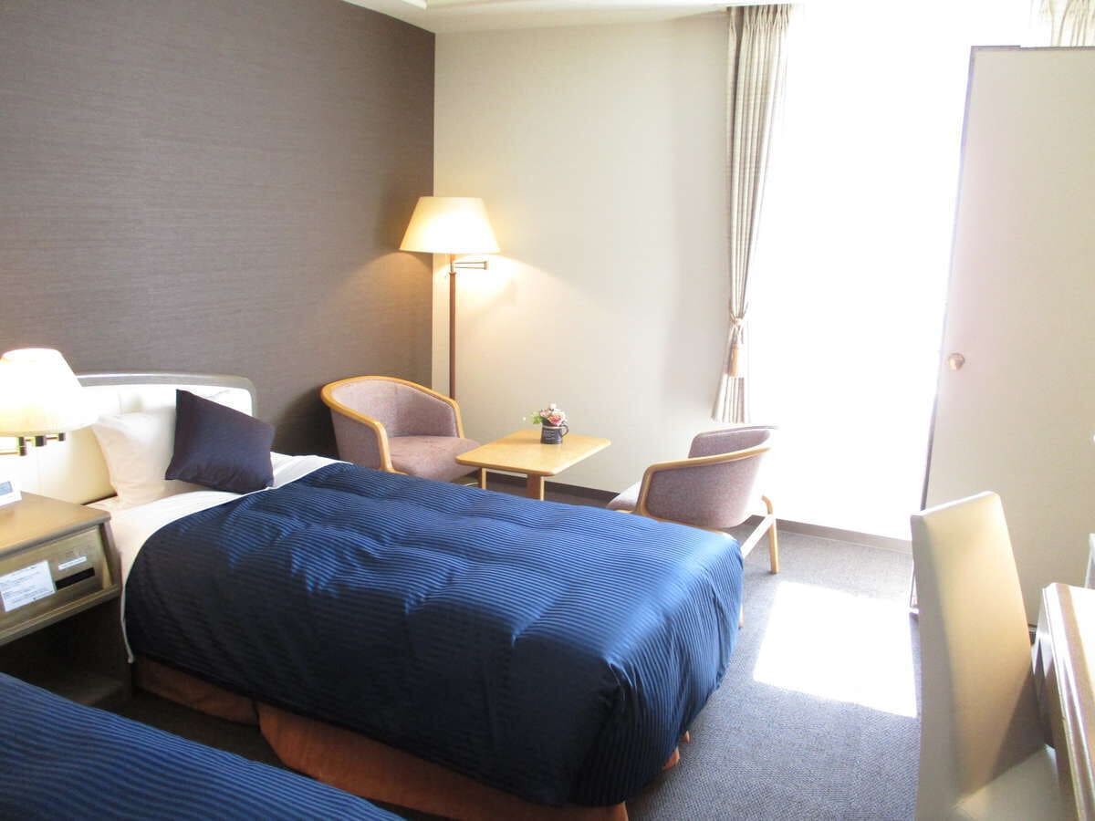 Habitación de hotel con una cama grande, dos sillas, una mesita, una lámpara y un escritorio con lámpara.