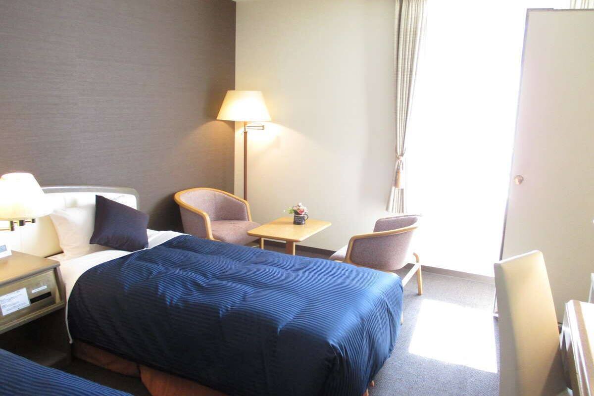 Une chambre d’hôtel avec un grand lit, deux chaises, une petite table, une lampe et un bureau avec une lampe.