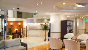 A modern hotel lobby with a reception desk, seating area, and a vending machine. - HOTEL LiVEMAX Sapporo Nakajima Park GRANDE (Sapporo)