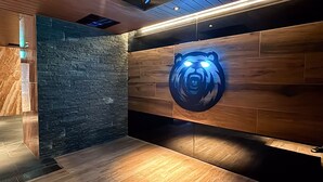 A modern interior with a stone wall and wooden paneling, a bear logo illuminated on the wall, and a vent on the floor. - HOTEL LiVEMAX Sapporo Nakajima Park GRANDE (Sapporo)