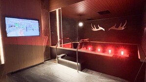 A room with a television displaying a news program, a wooden ceiling, and a wall with a lighted shelf. - HOTEL LiVEMAX Sapporo Nakajima Park GRANDE (Sapporo)
