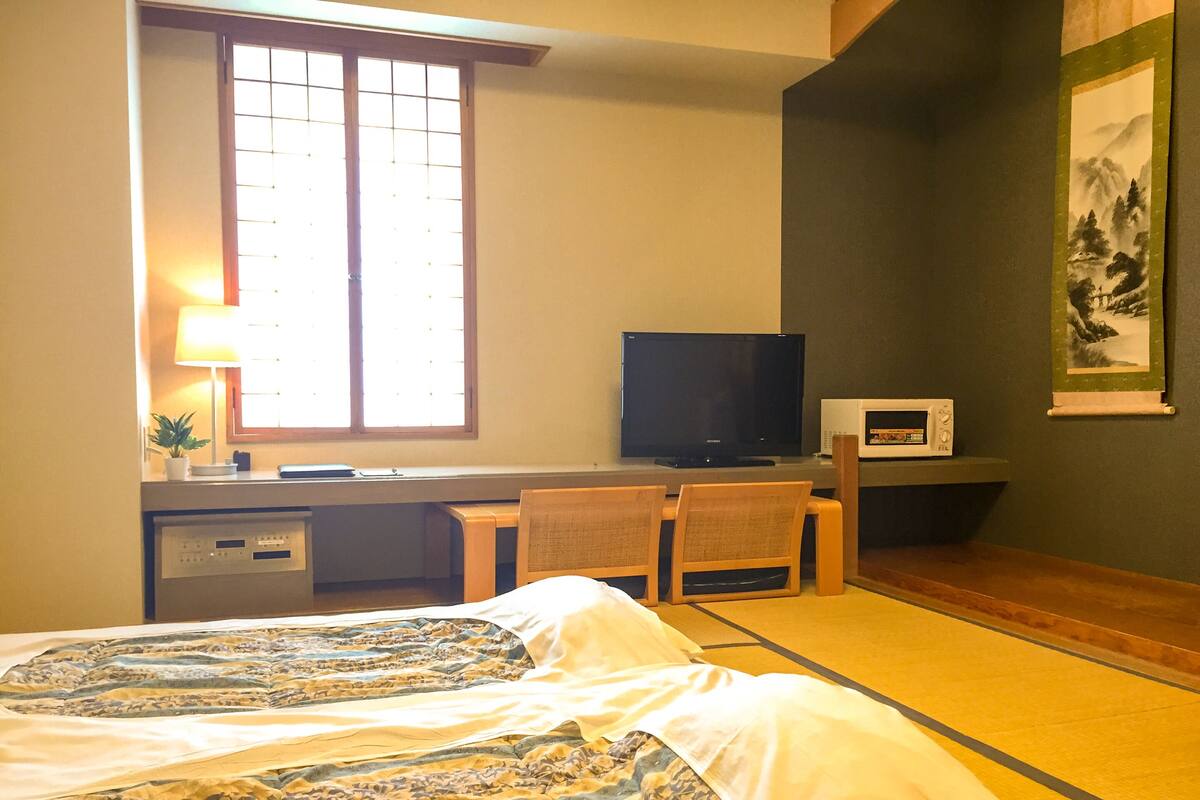 A hotel room with a bed, a desk with a television, a microwave, and a chair.
