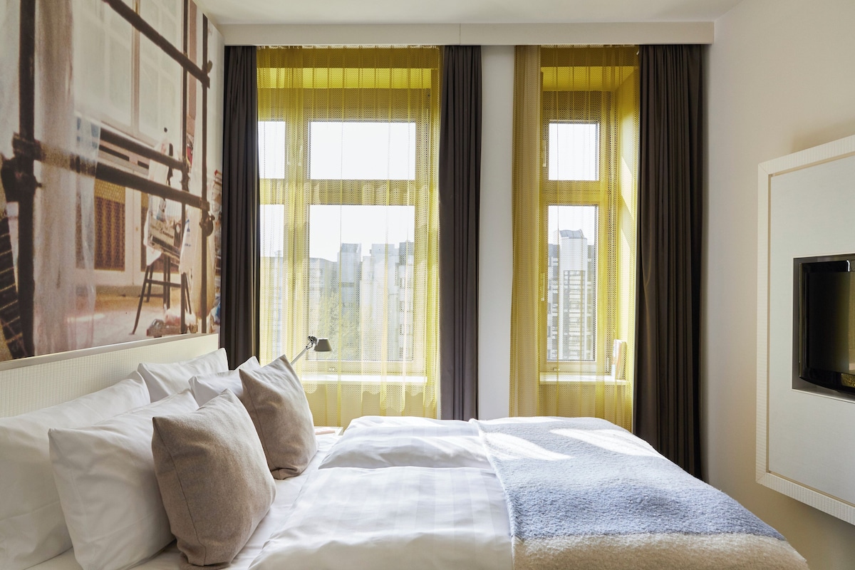 Une chambre d’hôtel avec un grand lit, un téléviseur à écran plat fixé au mur et une vue sur la ville par les fenêtres.