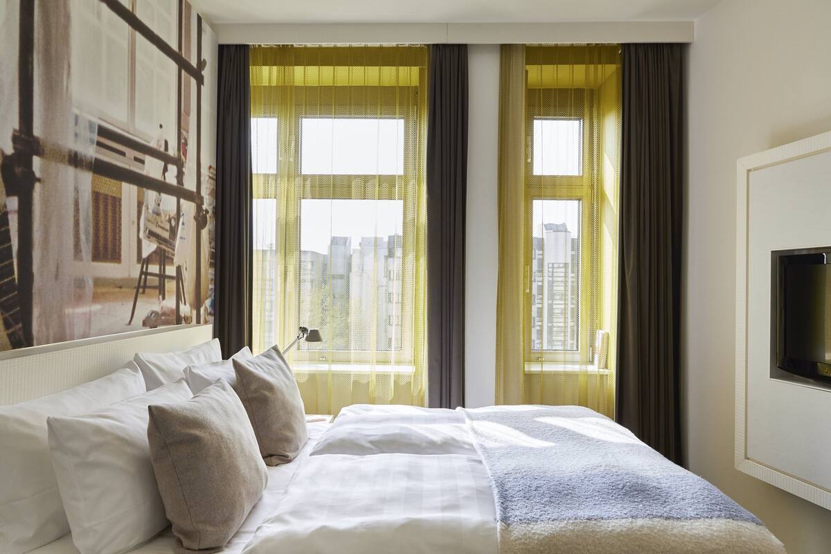 Une chambre d’hôtel avec un grand lit, un téléviseur à écran plat fixé au mur et une vue sur la ville par les fenêtres.